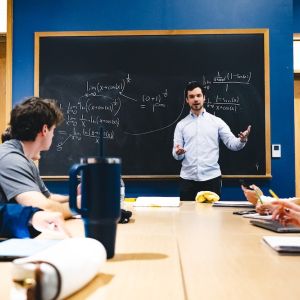Isaac Reiter stands in front of a blackboard and tutors students.
