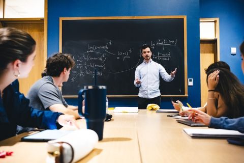 Isaac Reiter stands in front of a blackboard and tutors students.