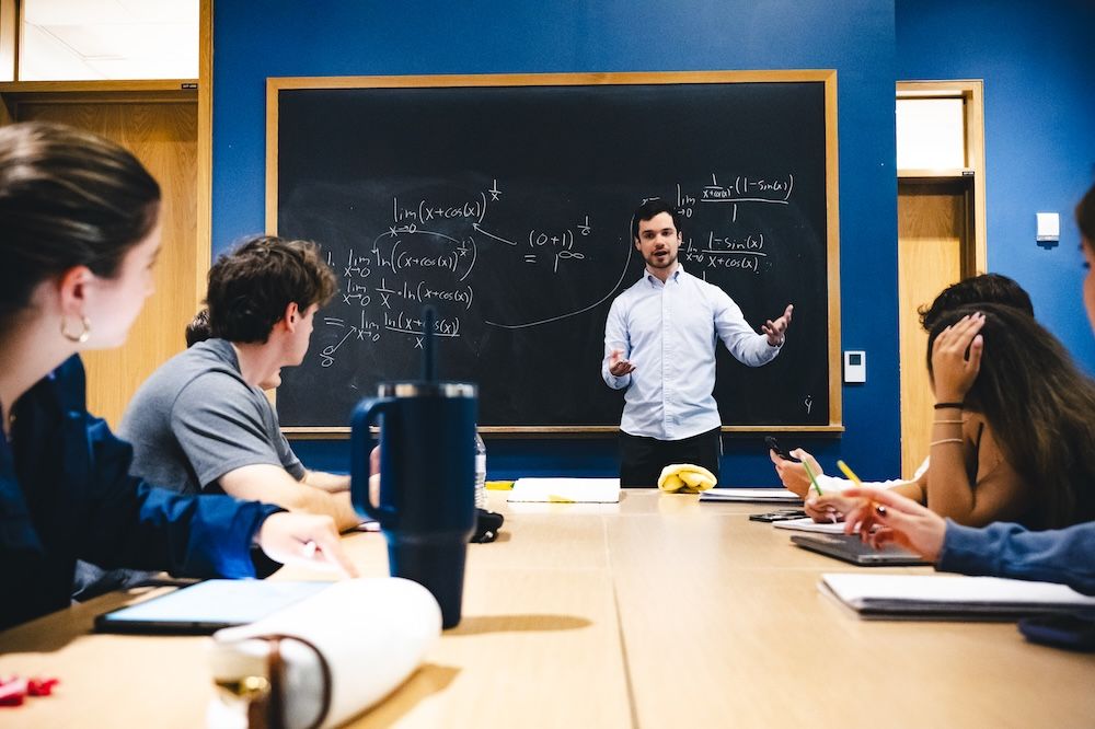 Isaac Reiter stands in front of a blackboard and tutors students.